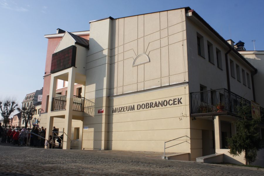 Betonowy budynek, na którym znajduje się metalowy napis: „Muzeum Dobranocek”. Przed wejściem stoi tłum ludzi.