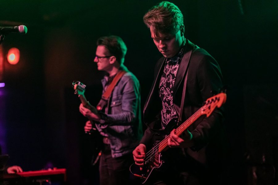 Na pierwszym planie Stefan Nowakowski daje koncert na gitarze basowej, na drugim planie Łukasz Borowicki gra na gitarze elektrycznej.