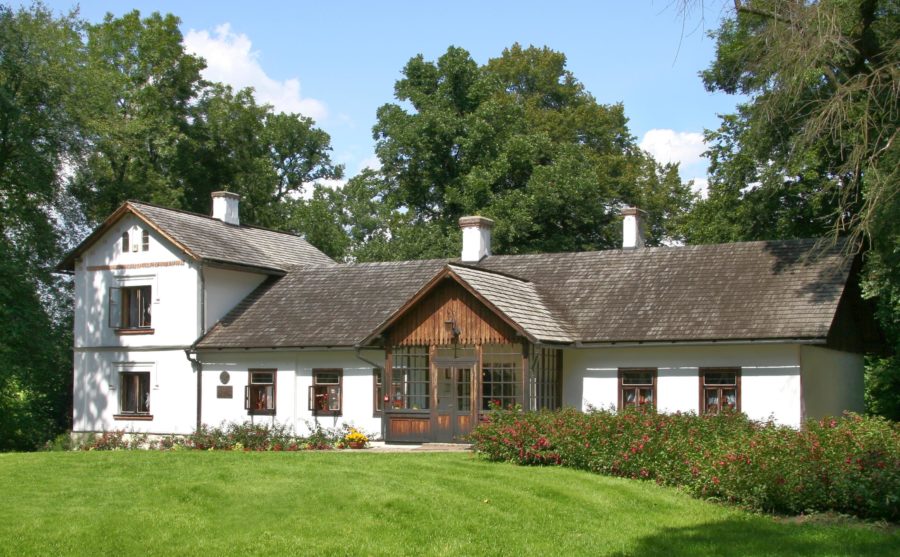 Dworek Marii Konopnickiej. Budynek o jasnych ścianach i ciemnym dachu. Wokół domu jest wiele roślinności.
