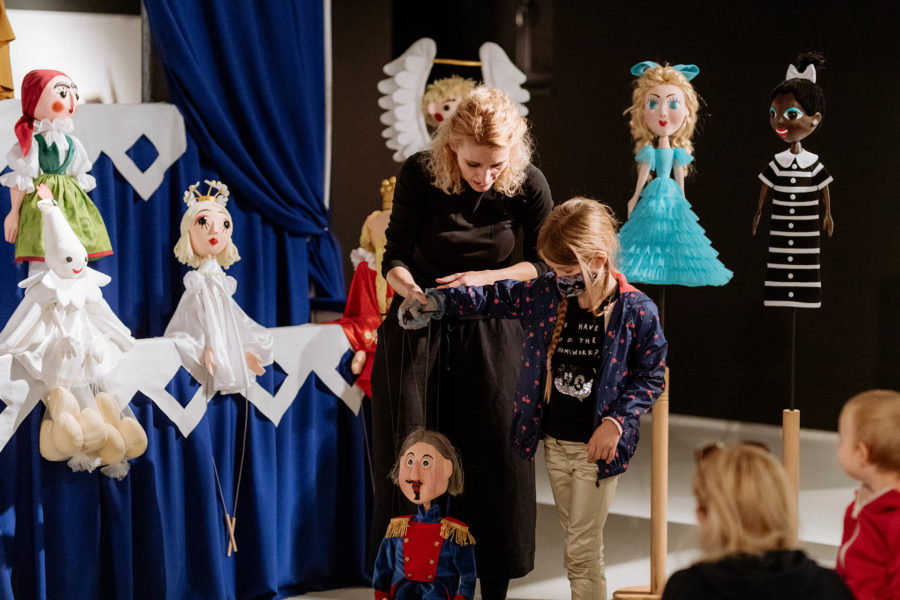 Kobieta na scenie uczy kilkuletnią dziewczynkę jak poruszać marionetką.