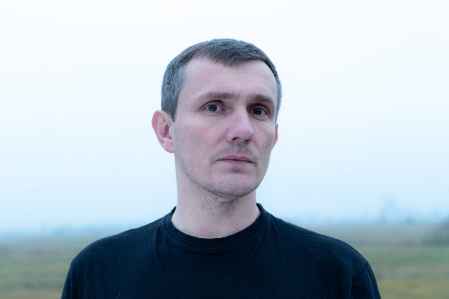 Portret mężczyzny w średnim wieku, który pozuje na tle zamglonego pola.