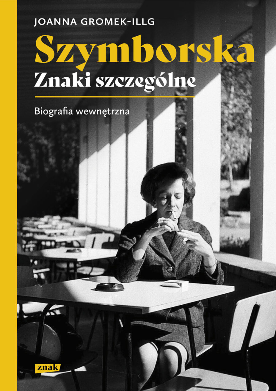 Okładka książki pod tytułem: "Wiesława Szymborska, Znaki szczególne", przedstawia bohaterkę biografii, która siedzi przy stoliku w pustej kawiarni i pali papierosa.