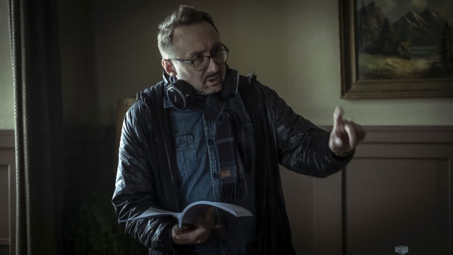 Mężczyzna instruuje kogoś nieujętego w kadrze. W jego prawej ręce znajduje się scenariusz.
