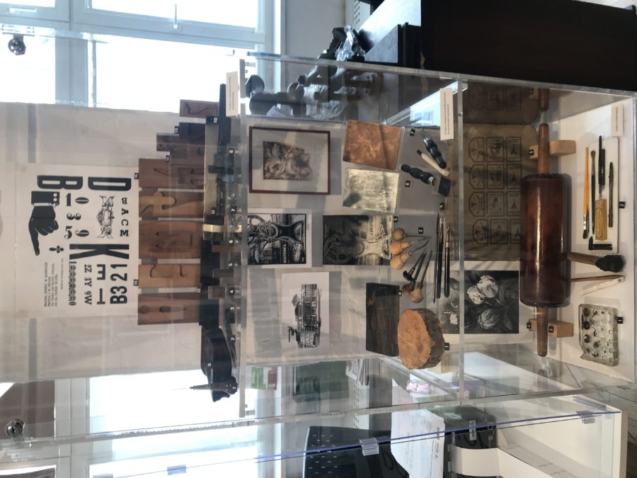 Przeszklona gablota, w której znajdują się drobne narzędzia oraz fotografie - fragment ekspozycji.
